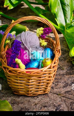 Ein Korb für eine Eiersuche dekoriert. Es hat Eier in Farbe Zinnfolie eingewickelt, ein Spielzeug von einem Kaninchen und einige Kugeln aus Garn. Es ist von Vegetation umgeben, cl Stockfoto