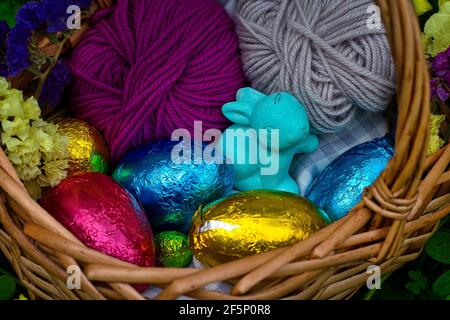 Ein Korb für eine Eiersuche dekoriert. Es hat Eier in Farbe Zinnfolie eingewickelt, ein Spielzeug von einem Kaninchen und einige Kugeln aus Garn. Es ist von Vegetation umgeben, cl Stockfoto