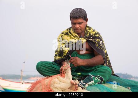 Weligama, Sri Lanka - März 28 2019: Ein lokaler Sri-lankischer Fischer sitzt untangling Fangnetz am Weligama Beach, an der Südküste von Sri Lanka. Stockfoto