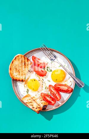 Zwei Spiegeleier mit Toast mit Avocado-Scheiben und Gemüse auf buntem Hintergrund. Frühstückskonzept. Gesundes vegetarisches Essen. Nahaufnahme, Kopierbereich Stockfoto