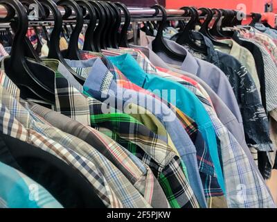 Reihe von riesigen Zahlen von bunten Hemden auf Kleiderbügel in Second Hand Store. Das Konzept des billigen Einkaufens, schwarzer Freitag. Stockfoto