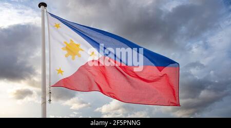 Philippinen Zeichen Symbol. Republik der Philippinen Nationalflagge auf einer Stange winkt gegen bewölkten Himmel Hintergrund. Stockfoto