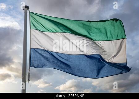 Sierra Leone Zeichen Symbol. Sierra Leone Nationalflagge auf einer Stange winkt gegen bewölkten Himmel Hintergrund. Stockfoto