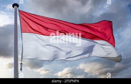 Indonesien Zeichen Symbol. Indonesische Nationalflagge auf einer Stange winkt vor bewölktem Himmel Hintergrund. Stockfoto