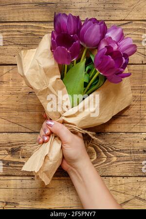 Hand mit lila Tulpen Bouquet in Bastelpapier auf Holz Nahaufnahme des Tisches Stockfoto