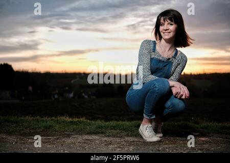 Ein Außenportrait einer jungen Frau, die Latzhose trägt Die Landschaft Stockfoto