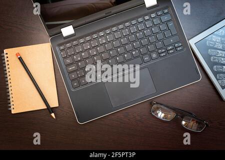 Arbeitsplatz mit Laptop, E-Book-Reader, Notizblock, Bleistift und Brille auf dunklem Holzhintergrund. Geschäfts- und Bildungskonzept. Stockfoto