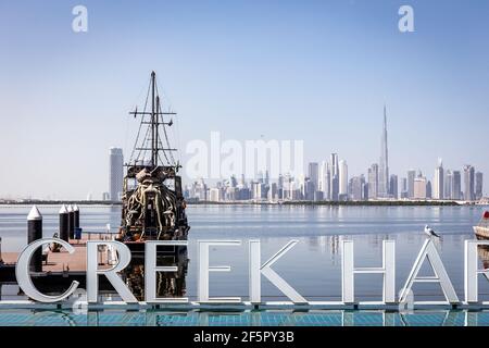 Dubai, VAE, 22,02.2021. Dubai Creek Hafenschild mit Black Pearl Piratenschiff mit Tour mit Dubai Downtown Skyline im Hintergrund. Stockfoto