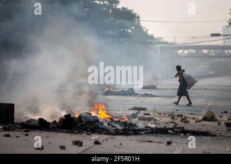 Yangon, Myanmar. März 2021, 27th. Ein Flaschenpflücker, der während der Demonstration an den brennenden Reifen vorbeifährt. Myanmar Militär greift Demonstranten mit Gummigeschossen, lebender Munition, Tränengas und Schallbomben als Reaktion an. Die Zahl der Todesopfer beträgt heute 144 und die höchste Zahl der Todesopfer seit dem Militärputsch im Februar 1. (Foto von Theint Mon Soe/SOPA Images/Sipa USA) Quelle: SIPA USA/Alamy Live News Stockfoto