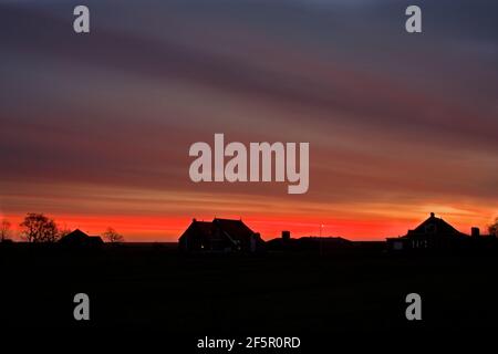 Feuriger Himmel über Silhouetten von Bauernhäusern vor Sonnenaufgang auf der Niederländische Insel Terschelling Stockfoto