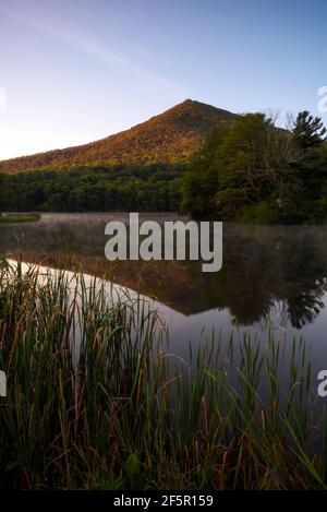 Am frühen Morgen trifft Licht auf die Ostseite des Sharp Top Mountain, während Nebel aus der Reflexion im Abbott Lake bei Peaks of Otter aufsteigt. Stockfoto