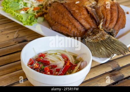 Traditionelle thailändische Küche, gegrillter Fisch und Suppe auf einem Bambustisch. Stockfoto