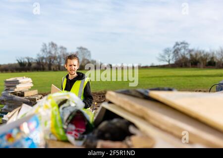 Ein junger erwachsener männlicher Baumeister trägt eine gut sichtbare Weste Werfen Müll in einen sprung Stockfoto