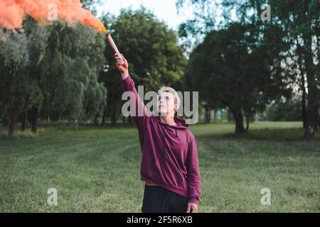 Mann im Street Style im Hoodie hält Hand Flare mit roter Rauchgranatenbombe. Stockfoto