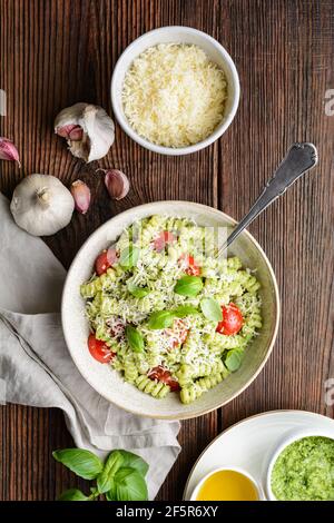 Fusilli Pasta mit Basilikum Pesto Sauce und Kirschtomaten, bestreut mit zerkleinerten Käse auf rustikalem Holzhintergrund Stockfoto