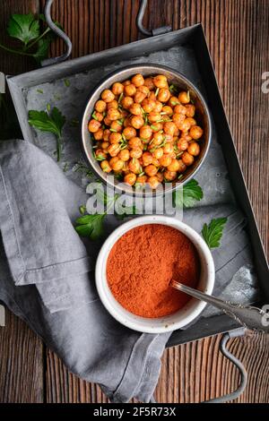 Knackiger Snack, knusprig und würzig im Ofen geröstete Kichererbsen mit Paprika und rotem Chilipulver auf rustikalem Holzhintergrund Stockfoto