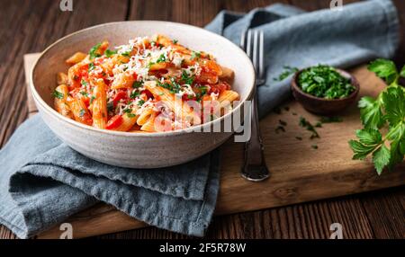 Klassische Penne all'Arabiata, würzige Pasta mit Tomaten und Chilisauce, gekrönt mit geriebenem Käse auf rustikalem Holzhintergrund Stockfoto