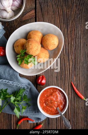 Hausgemachte klassische Arancini Di Riso, knusprige sizilianische Reisbällchen gefüllt mit Mozzarella Käse, serviert mit heißen Arrabbiata Dipping Sauce auf rustikalem Holz Stockfoto