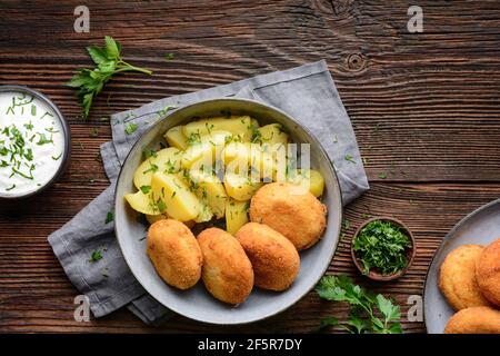 Gebratener Blumenkohl- und Käsebroketten mit gekochten Kartoffeln und sauer Creme Dip auf rustikalem Holzhintergrund Stockfoto