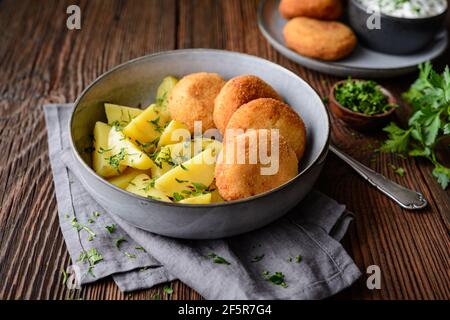 Gebratener Blumenkohl- und Käsebroketten mit gekochten Kartoffeln und sauer Creme Dip auf rustikalem Holzhintergrund Stockfoto