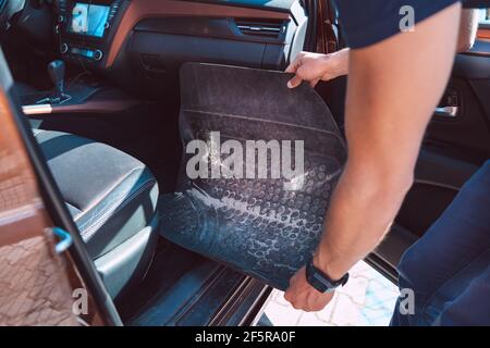 Mann, der aus dem Auto schmutzigen Gummi matt oder Teppich vor dem Staubsaugen. Reinigung Auto innen Stockfoto