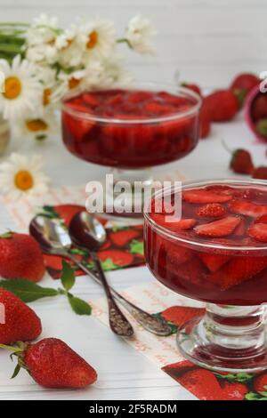 Gelee aus frischen Erdbeeren in zwei Tassen auf weißem Hintergrund und Bouquet von Kamillen. Vertikales Format Stockfoto