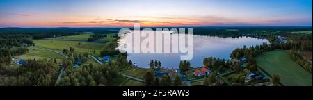 Luftlandschaftliches Panorama der Mitternachtssonne in Nordschweden, mittelsommerliche helle Nächte, Polarregion. Rot-orange Himmel, blauer See, schwedische Häuser bei coas Stockfoto