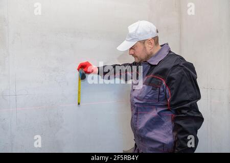 Ein Mann, ein Elektriker markiert mit Bleistift, Maßband und einer linearen Ebene zum Bohren von Löchern für Steckdosen Stockfoto