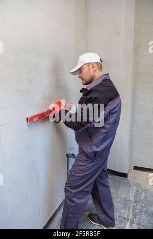 Ein Mann, ein Elektriker markiert mit Bleistift, Maßband und einer linearen Ebene zum Bohren von Löchern für Steckdosen Stockfoto