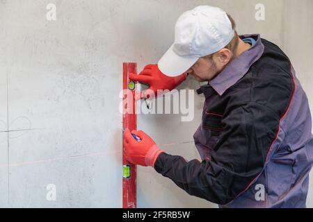 Ein Mann, ein Elektriker markiert mit Bleistift, Maßband und einer linearen Ebene zum Bohren von Löchern für Steckdosen Stockfoto