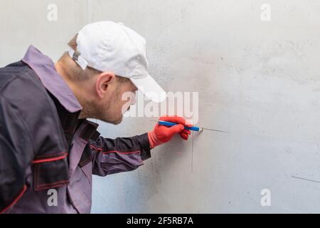 Ein Mann, ein Elektriker markiert mit Bleistift, Maßband und einer linearen Ebene zum Bohren von Löchern für Steckdosen Stockfoto