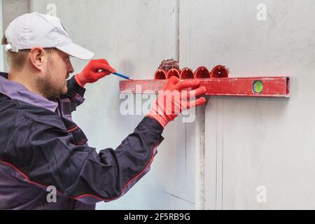 Ein Mann, ein Elektriker markiert mit Bleistift, Maßband und einer linearen Ebene zum Bohren von Löchern für Steckdosen Stockfoto