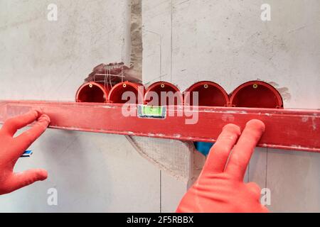 Ein Mann, ein Elektriker markiert mit Bleistift, Maßband und einer linearen Ebene zum Bohren von Löchern für Steckdosen Stockfoto