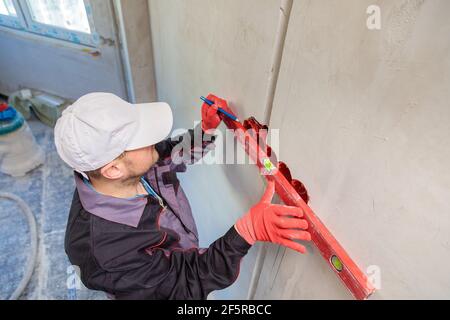 Ein Mann, ein Elektriker markiert mit Bleistift, Maßband und einer linearen Ebene zum Bohren von Löchern für Steckdosen Stockfoto