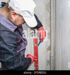 Ein Mann, ein Elektriker markiert mit Bleistift, Maßband und einer linearen Ebene zum Bohren von Löchern für Steckdosen Stockfoto