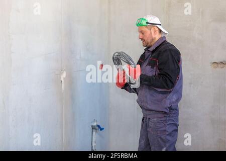 Ein Elektriker steht mit einem elektrischen Kabel für Steckdosen gegen die Wand. Nahaufnahme Stockfoto