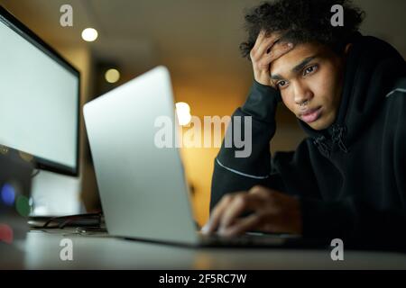 Müde junge Kerl studieren oder arbeiten auf Laptop, sitzen in dunklen Raum zu Hause spät in der Nacht Stockfoto