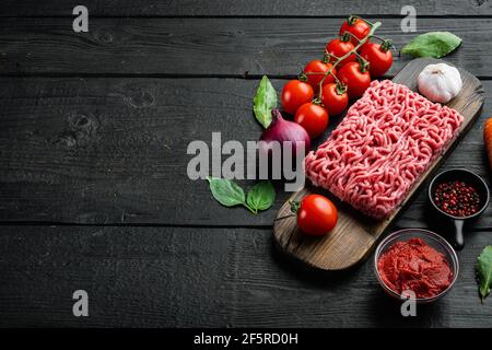 Zutaten für Bolognese-Sauce, Hackfleisch, Tomaten, Kräuter-Set, auf Holzschneidebrett, auf schwarzem Holztisch-Hintergrund, mit Platz für Kopien Stockfoto