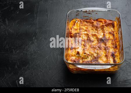 Italienisches Essen. Hot Tasty frisch gebackene Lasagne Set, in Backblech, auf schwarzem Stein Hintergrund, mit Platz für Text Stockfoto