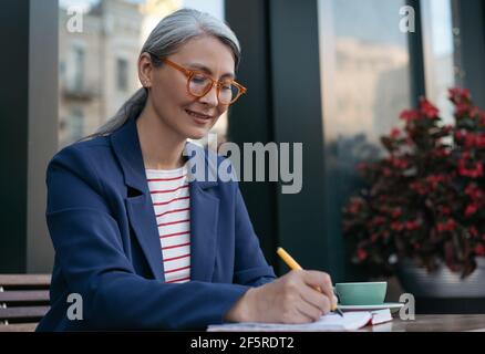 Reife Geschäftsfrau tragen stilvolle Brillen Arbeitsprojekt, Planung Startup. Portrait des asiatischen Schriftstellers, der Notizen gemacht hat. Erfolgreiches Geschäft Stockfoto