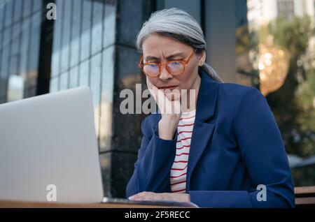 Müde asiatische Geschäftsfrau arbeiten Projekt, mit Laptop, Suche nach Informationen. Porträt der frustrierten reifen Frau am Arbeitsplatz sitzen Stockfoto