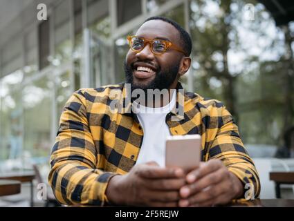 Junge gut aussehende afroamerikanische Mann in stilvollen Brillen halten Handy, Kommunikation online Stockfoto