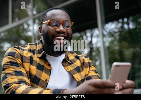 Afrikanischer Mann mit Handy. Emotionaler Kerl hält Smartphone, Video ansehen Stockfoto