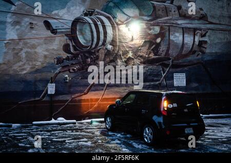 Ein kleines Auto, das während eines Wintereissturms in der Stadt Richmond, Virginia, in den USA, vor einem Wandbild einer Raumstation mit einleuchteten Lichtern geparkt war. Stockfoto