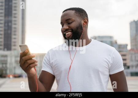 Gutaussehender Kerl mit Handy, Kommunikation, zu Fuß auf der Straße. Afroamerikanischer Mann hält Smartphone und hört im Freien Fehlstellen Stockfoto