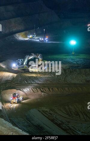 Tagebaubetrieb in der Nacht mit Bohrgeräten, Muldenkipper und Ladern, die unter Flutlicht betrieben werden. Stockfoto