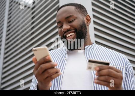 Nahaufnahme Porträt von lächelnden afrikanischen Mann mit Kreditkarte, mit modernen mobilen App-Shopping online Stockfoto