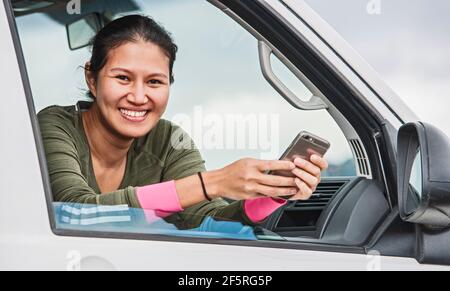 Frau schreibt auf ihrem Smartphone, während sie in ihrem Van sitzt Stockfoto