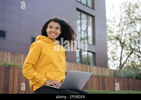 Schöne lächelnde afroamerikanische Frau mit Laptop-Computer, arbeitet freiberuflich Projekt. Porträt eines jungen selbstbewussten Designers, der am Arbeitsplatz sitzt Stockfoto