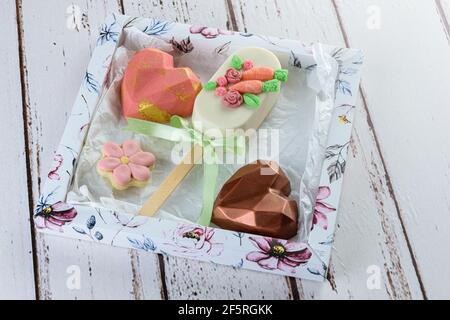 Karottenkuchen-Cakesicle, umgeben von herzförmiger Schokolade und blumenförmigem Keks. Auf einem weißen Feld. Stockfoto